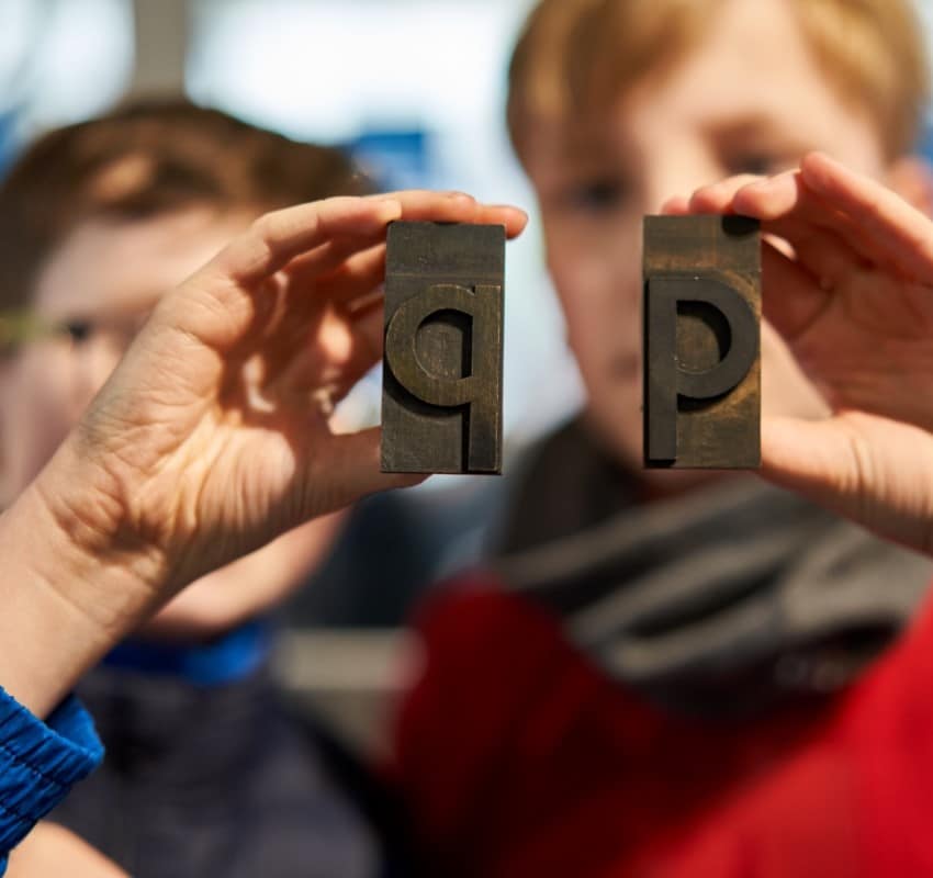 Children hold up a P and Q in lowercase type - mind your ps and qs!