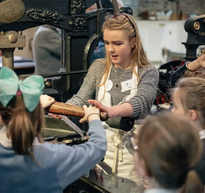 Instructor showing rpimary shcool students how to use the print machine