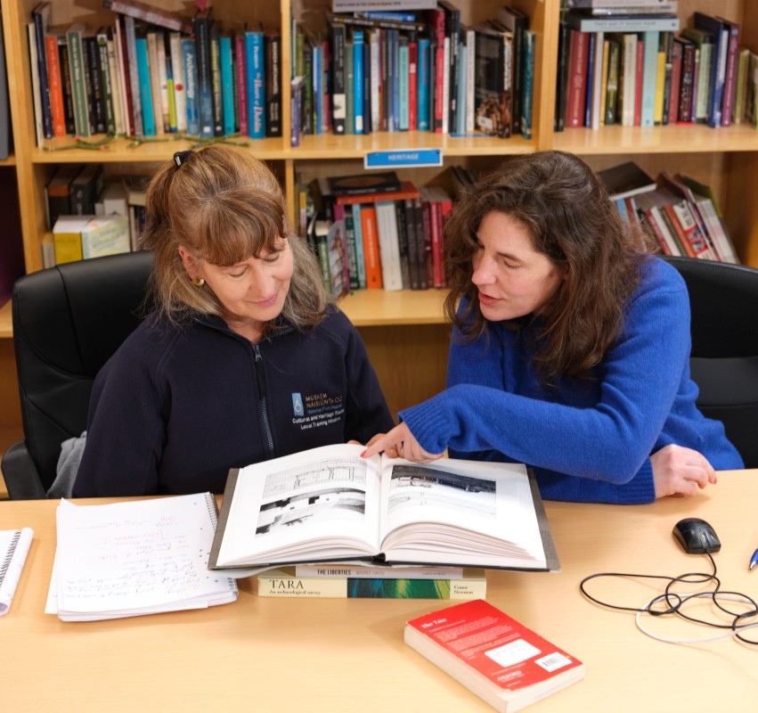 two learners read through a textbook together while sitting at a desk
