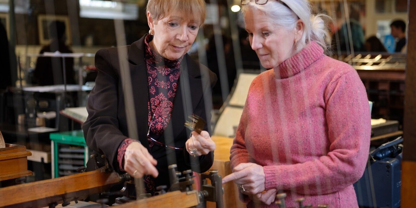 A tour guide gestures to show how the Shaw Pen Ruling machine operates