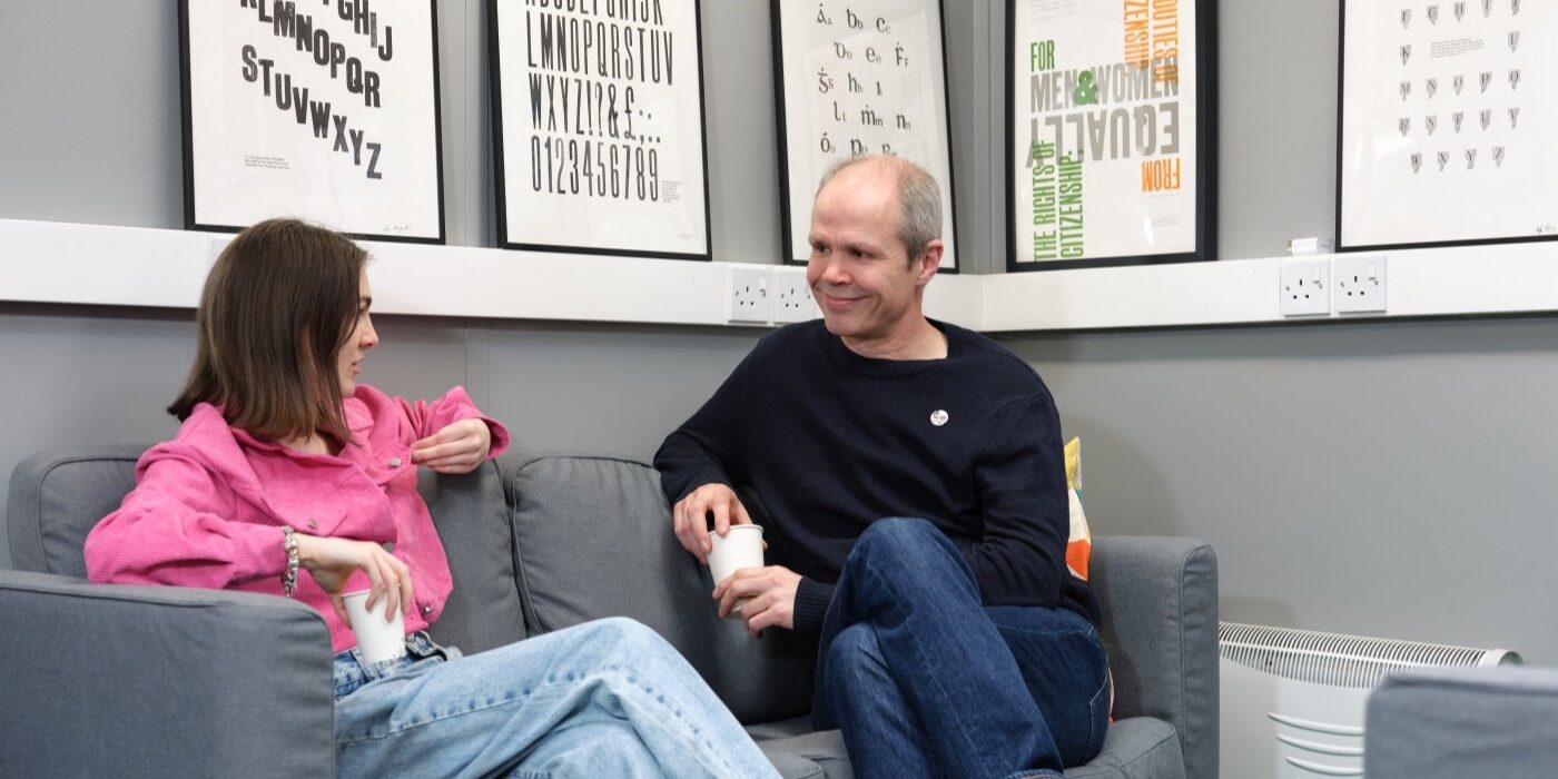 two learners sit on couches and chat while drinking coffee