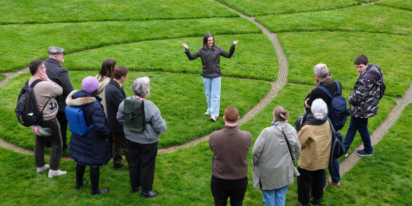 A tour guide in a green, grassy park speaking to the tour attendees