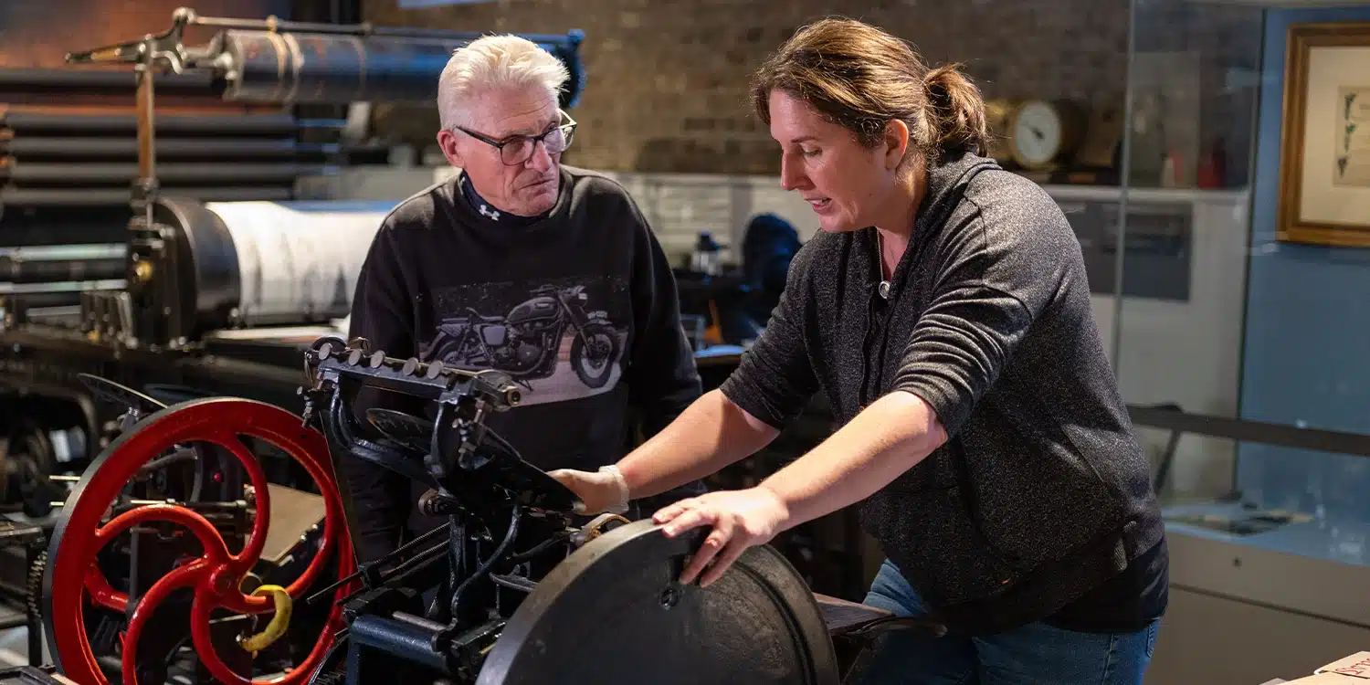 Woman working at printer while person observes