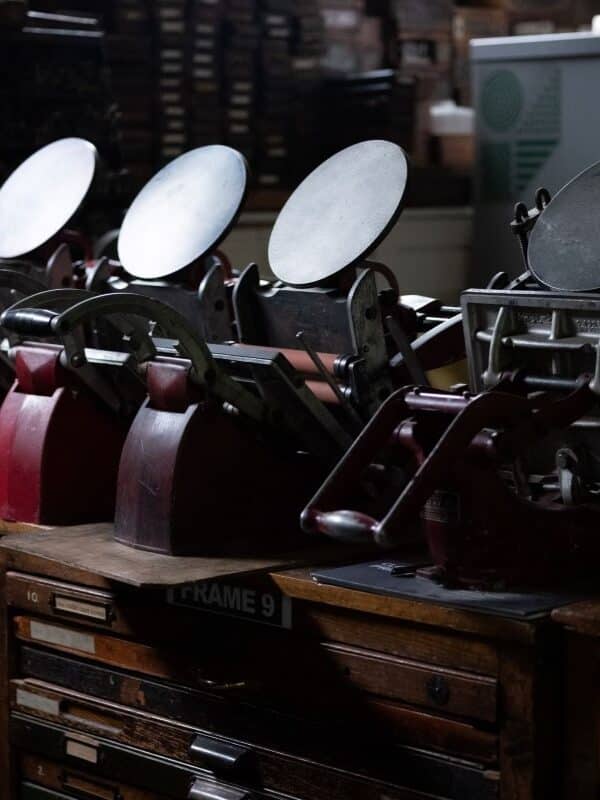 Four tabletop Adana printing presses in a row on top of cases of type.