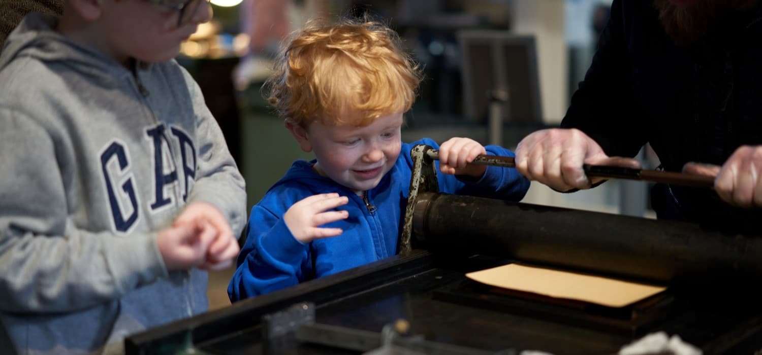 Children trying out a proofing press during a family tour