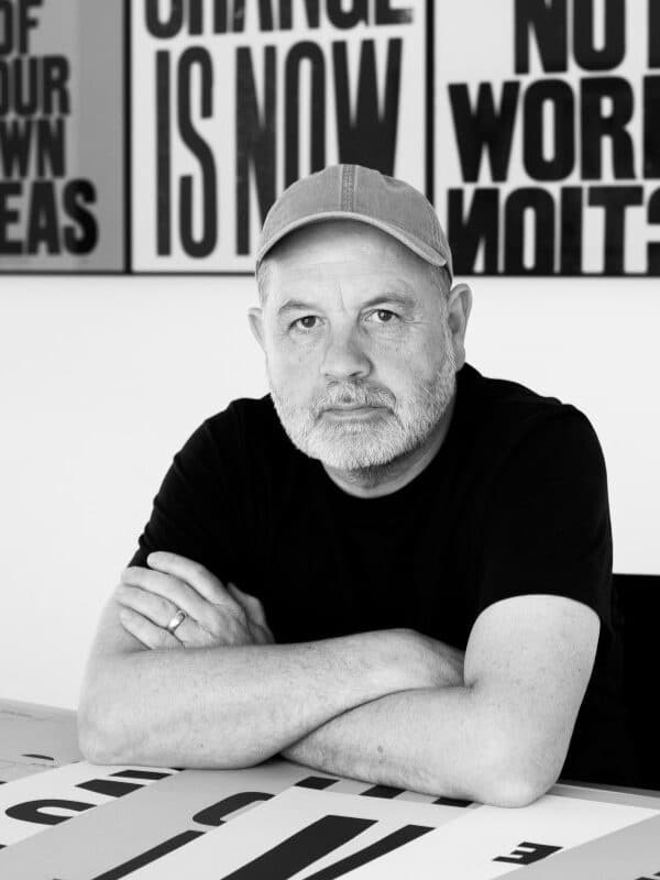 A photo of artist Anthony Burrill surrounded by some of his works