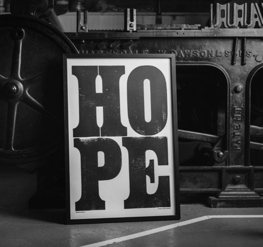 Anthony Burrill's print HOPE, framed and propped against a printing press