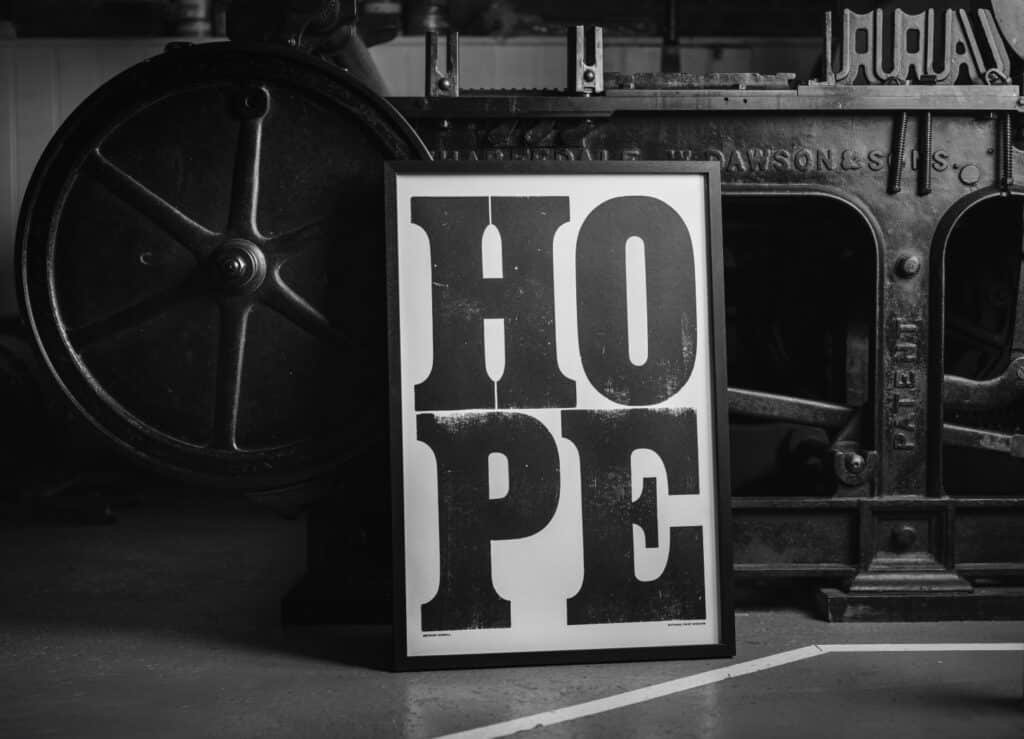 A framed version of Anthony Burrill's HOPE print, propped up against the Wharfdale Stop Cylinder Press on which it was printed