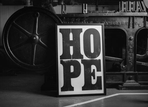 A framed version of Anthony Burrill's HOPE print, propped up against the Wharfdale Stop Cylinder Press on which it was printed