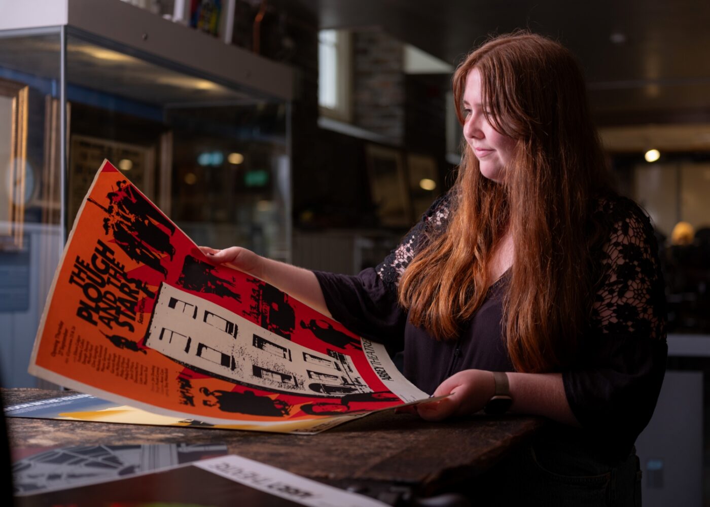 Niamh examines an orange and black poster for the play The Plough and the Stars