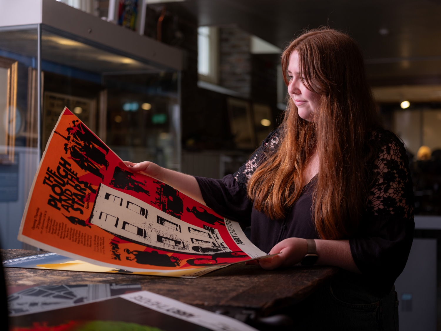 Niamh examines an orange and black poster for the play The Plough and the Stars
