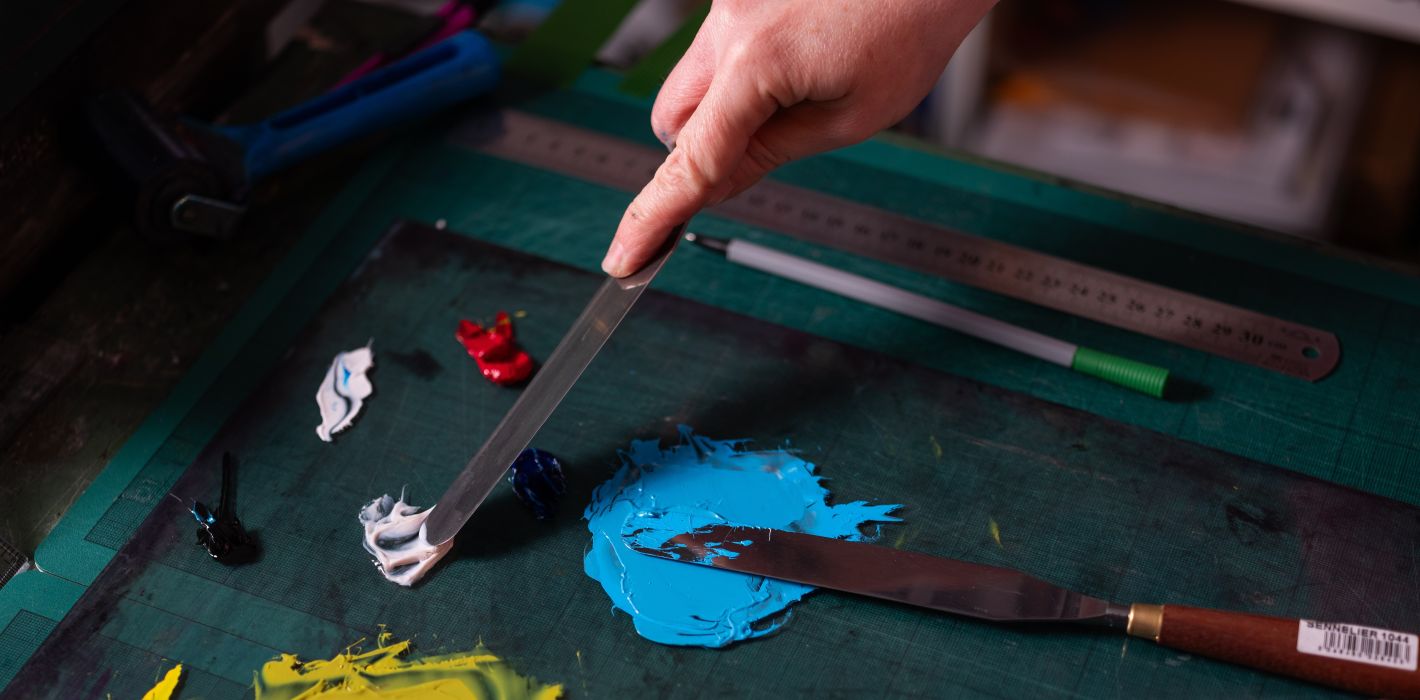 A printer mixes inks of various colours using a palette knife.