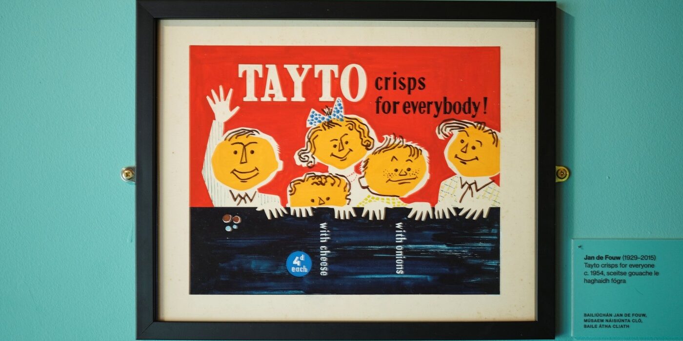 An advertisement for Tayto crisps framed and hanging against a turquoise background.