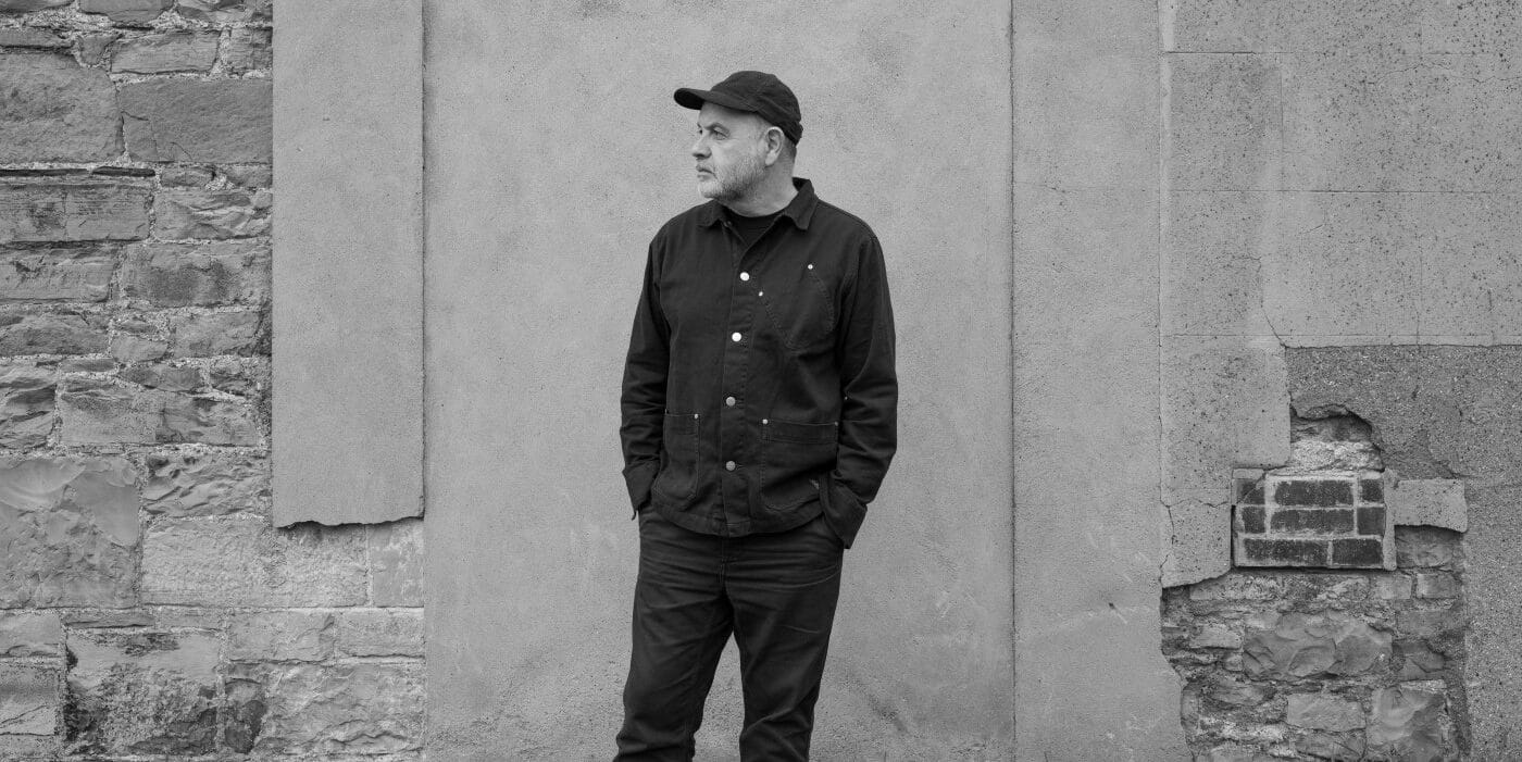 A photograph of artist Anthony Burrill standing in front of a stone wall.