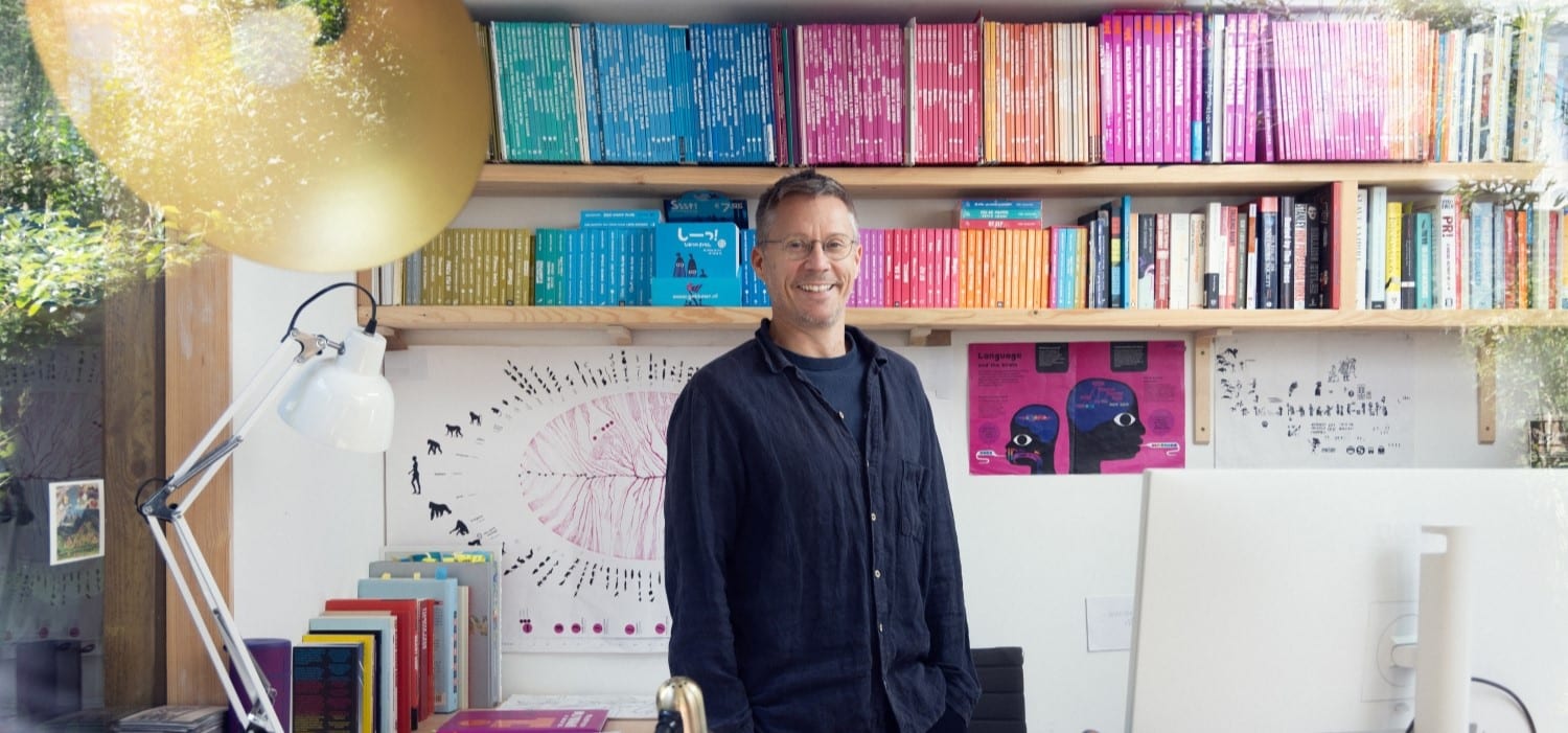 A photograph of author Chris Haughton standing in front of a shelf of colourful books.