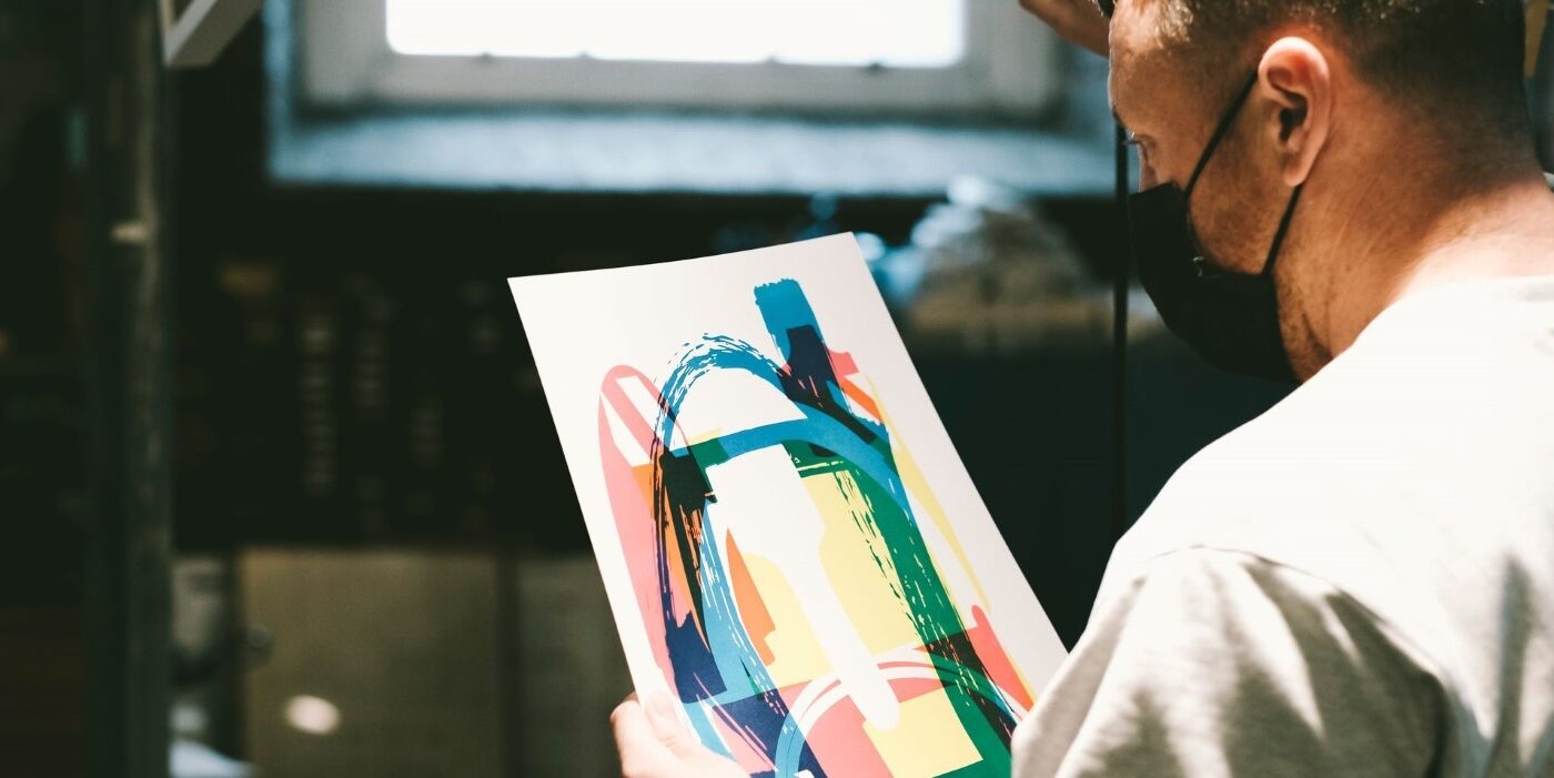 The artist Maser wearing a mask looks down at a proof of a print.