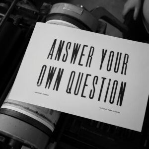 A letterpress print lying on a printing press which reads "Answer Your Own Question".