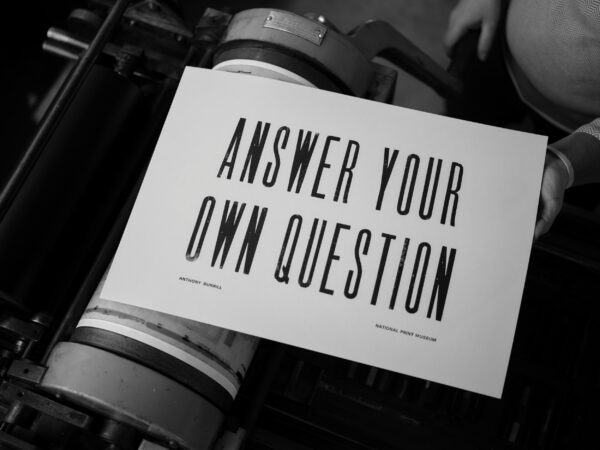 A letterpress print lying on a printing press which reads "Answer Your Own Question".