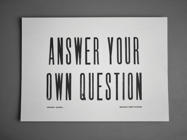 A letterpress print lying on a grey background which reads "Answer Your Own Question".
