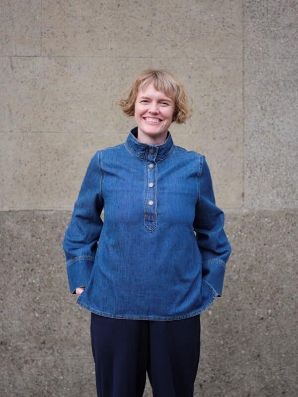 A photograph of Annie Atkins standing in front of a stone wall.