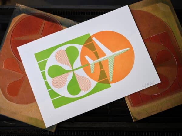 A letterpress print in orange and green of an airplane and a shamrock sits on top of printing plates.